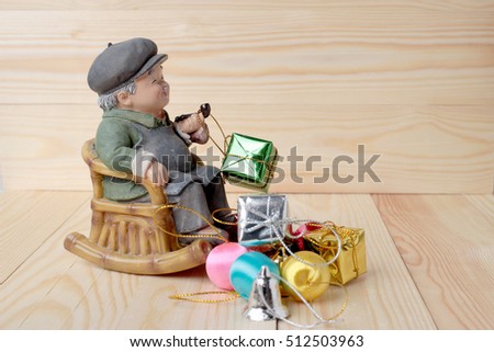 lovely grandparent doll siting rocking bamboo chair with gift boxes and gift decoration christmas on pine wooden background with copy space.