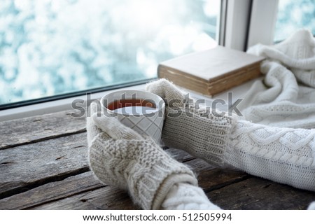 Female hands holding hot drink on windowsill