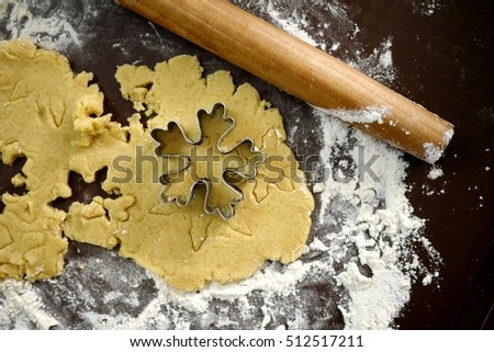 Top view photo of dough with rolling pin and cookie mold in the form of a snowflake. Snowflake shape cookies cutting forms.
