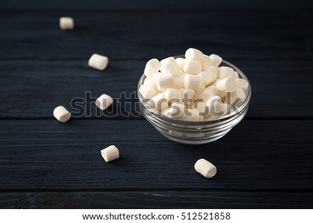 white marshmallows in a glass bowl on blue wooden background.