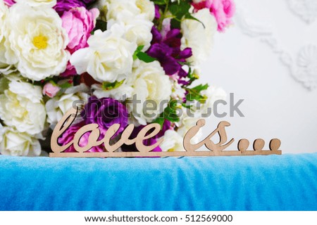 wooden words LOVE IS... against the background of a bouquet flowers