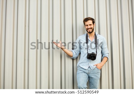 smiling man with his camera over his neck on gray background, showing one side