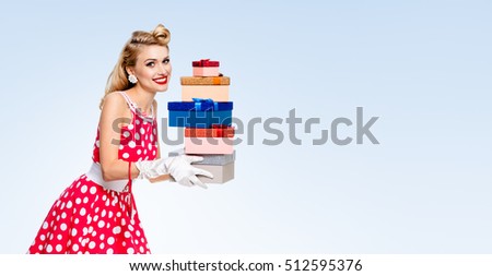 Happy woman in pin-up style red dress in polka dot, holding gift boxes, on blue, with blank copyspace area for advertise text or slogan. Caucasian model posing in retro fashion and vintage concept.