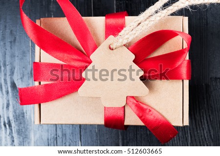 Pine tree label with twine attached on paper present with red ribbon bow. Black natural wooden table. Christmas gift abstract concept. 