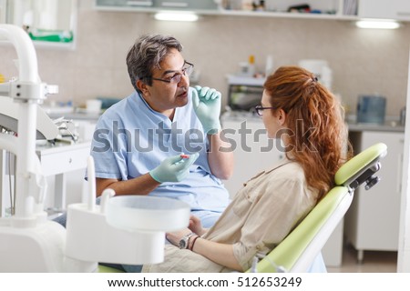 Senior male  dentist in dental office talking with female patient and preparing for treatment. Royalty-Free Stock Photo #512653249