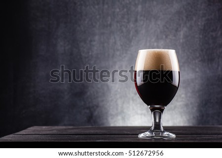 Glass of dark beer over a dark textured wooden background Royalty-Free Stock Photo #512672956