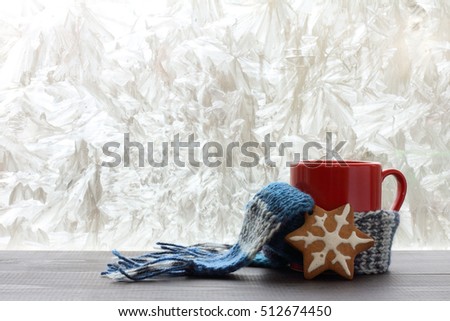red mug with a warm scarf and pastries in the background of a winter window / warming holiday mood