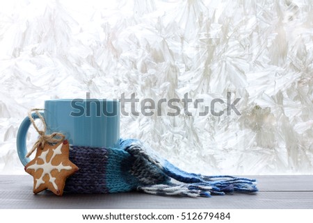 blue mug with a warm scarf and homemade cakes on the background of frozen window / drinks for the winter season