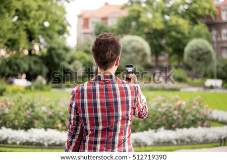 Man taking a photo with smart phone. Picture of beautiful building with blooming garden, tourist.