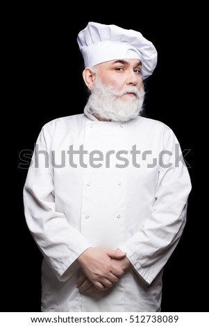 Bearded man cook in chef hat and uniform in studio on black background