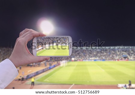 Hand with smart phone in a stadium taking pictures of a sport event