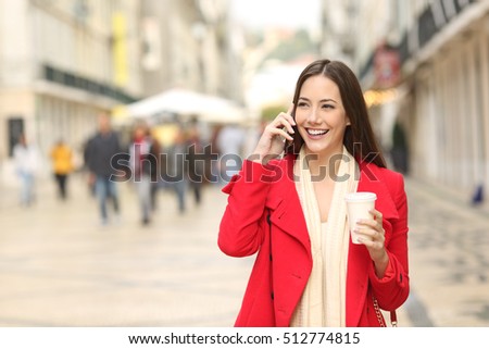 Front view portrait of a happy woman calling on the mobile phone walking towards camera in the street