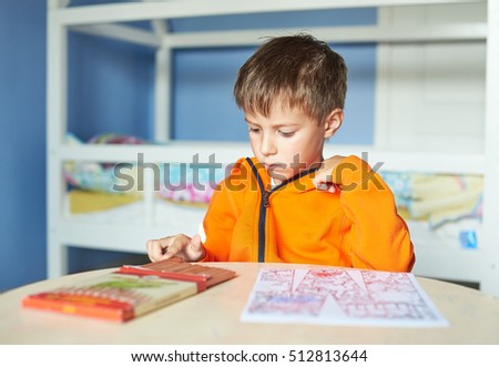 Boy is carefully drawing a picture with pencils. He is five years old. He is sitting at the table.