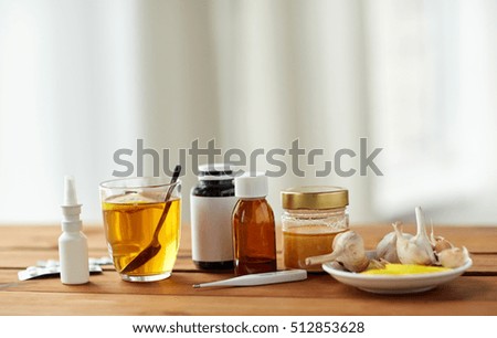 healthcare, traditional medicine and flu concept - drugs, thermometer, honey and cup of tea on wooden table Royalty-Free Stock Photo #512853628