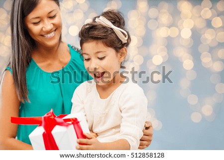 christmas, holidays, celebration, family and people concept - happy mother and child girl with gift box over lights background