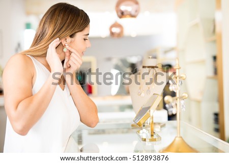 Profile view of a pretty young woman trying a pair of earrings in front of a mirror at a jewelry and fashion shop