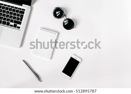 White office desk with laptop, smartphone, sunglasses and notebook . Top view with copy space, flat lay.
