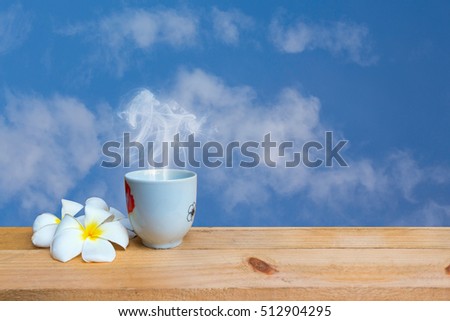 Coffee mug with smoke and flower on wood table on sky background.white cup of coffee or tea on wooden plate over blurred plantation of coffee tree with sun lighting.