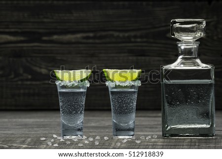 Two glasses  cold silver tequila with lime on a black wooden background