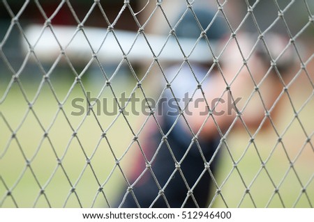 Baseball player out of focus behind baseball cage net. Royalty-Free Stock Photo #512946400