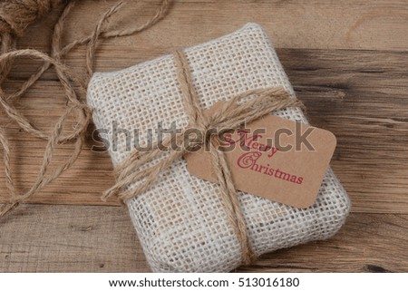 Closeup of a small fabric present with a Merry Christmas gift tag on a wood table.