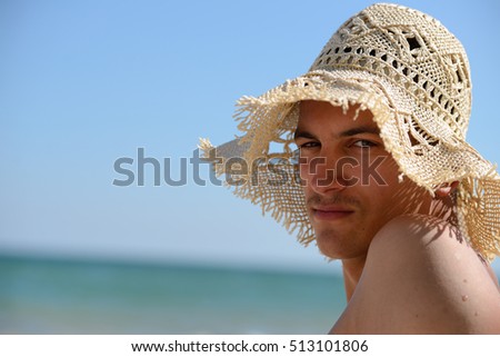 Funny picture of a relaxed young man with straw hat for woman stands to sunbath on the beach. Summer vacation. Sea in the background
