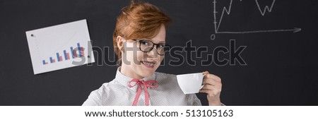 Pretty smart young woman holding cup of coffee on a blackboard background. Behind her charts with bar graphs