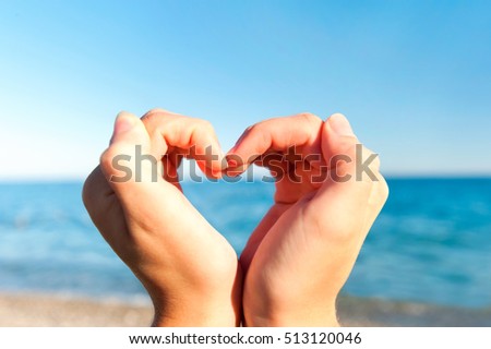 Composition finger frame- young woman's hands doing heart shape. Multicolored summertime horizontal outdoors inspirational image on blue sky background.