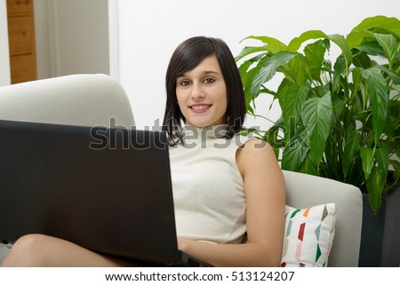 young brunette girl student sitting on the couch with a laptop