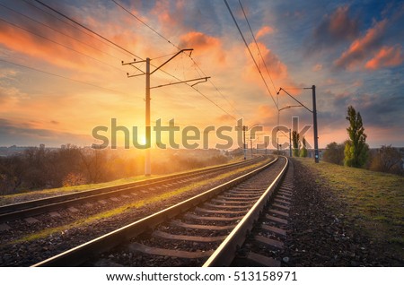 Railway station against beautiful sky at sunset. Industrial landscape with railroad, colorful blue sky with red clouds, sun, trees and green grass. Railway junction. Heavy industry. Evening in autumn Royalty-Free Stock Photo #513158971