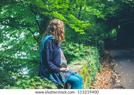 A young pregnant woman is sitting by the roadside in a forest