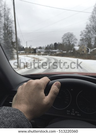 A business man is driving a modern car on a wintry road. The road is covered with snow and is slippery. Focus point on the hand. 