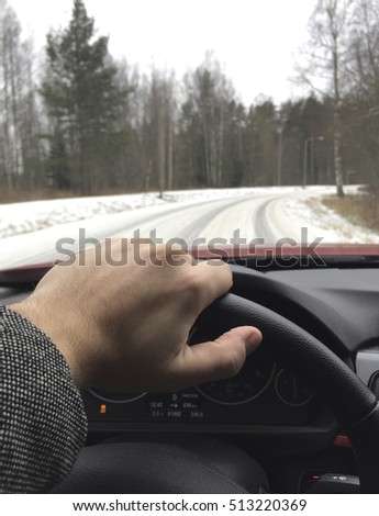 A business man is driving a modern car on a wintry road. The road is covered with snow and is slippery. Focus point on the hand. Traction control light is on.