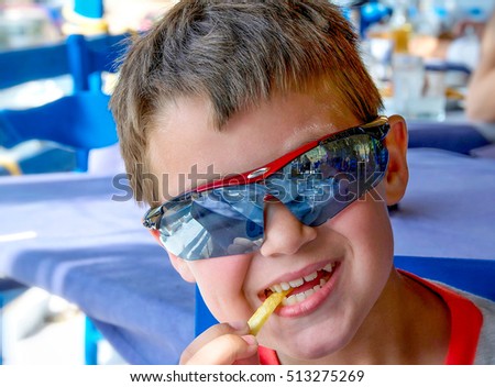 caucasian little boy with sunglasses eating unhealthy potatoes