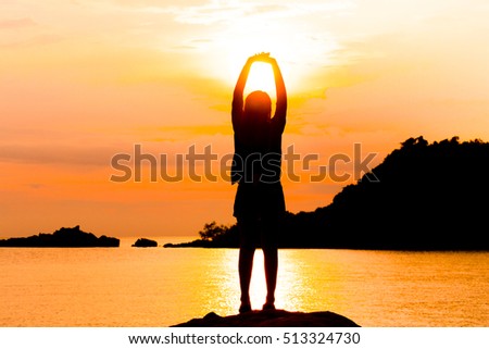 Silhouette of young woman standing at relax pose or freedom pose or chill pose on the beach during sunset.