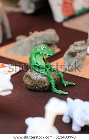 Paper Mache green frog craft is sitting on a rock among many other art work. Focused on frog.