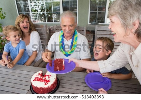 Senior woman serving slice of birthday cake at party with family