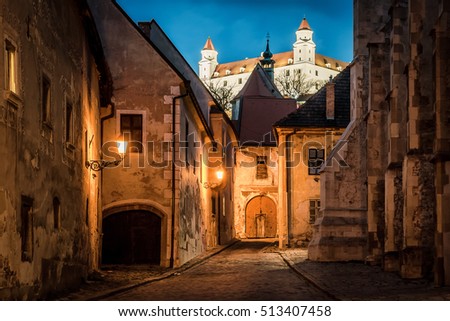 Night picture of old medieval street of Bratislava, Slovakia with illuminated castle in background.