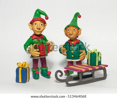Two little Christmas elf with gifts near sled. Plasticine characters on a white background