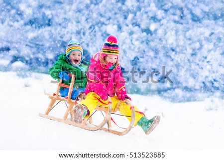 Little girl and boy enjoy a sleigh ride. Child sledding. Toddler kid riding a sledge. Children play outdoors in snow. Kids sled in Alps mountains in winter. Outdoor fun for family Christmas vacation.
