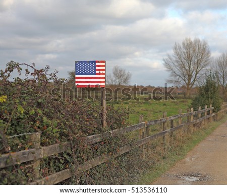A United States of America flag on a signpost along a deserted rural road.
