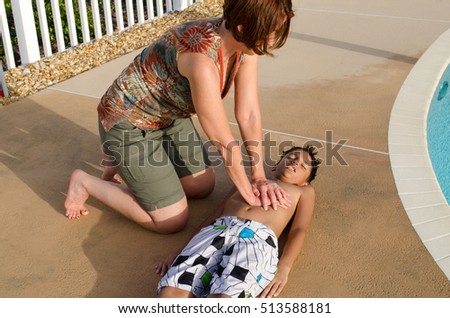 Woman performing cardiopulmonary resuscitation, known as car, on a young boy child who was in a state of medical emergency when he inhaled water while swimming at a swimming pool.