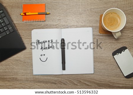 Open notebook with Spanish words "Buenas Tardes" ( Good Afternoon) and a cup of coffee on wooden background. Top down view
