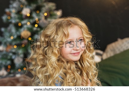 Portrait of pretty blonde little girl smiles and looks side in Christmas time