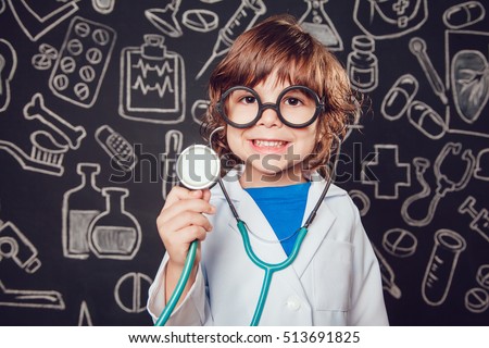 Happy little boy in doctor costume holding sthetoscope on dark background with pattern. The child has glasses Royalty-Free Stock Photo #513691825