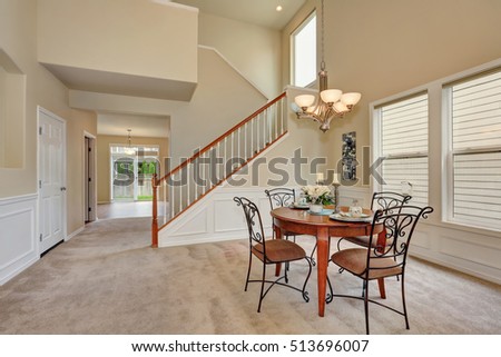 Beige dining room interior with high ceiling and staircase. Elegant table setting and wrought iron chairs. Northwest, USA