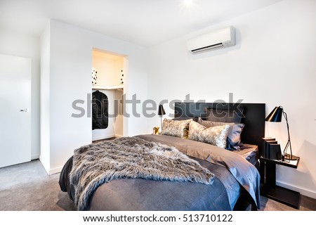 Dark and shiny decoration for a modern bed of a house or hotel, including a fur blanket and glossy pillows next to the dressing room
