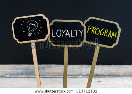 Concept message LOYALTY PROGRAM and light bulb as symbol for idea written with chalk on wooden mini blackboard labels, defocused chalkboard and wood table in background Royalty-Free Stock Photo #513712102