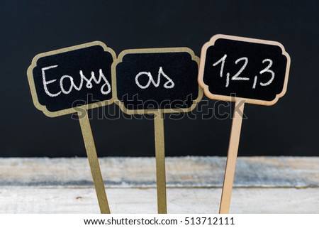Concept message EASY AS  written with chalk on wooden mini blackboard labels, defocused chalkboard and wood table in background