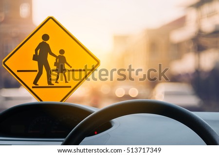 School zone warning sign and inside car view ,steering wheel on blur traffic road with colorful bokeh light abstract background. Copy space of transportation and travel concept. Vintage tone color.